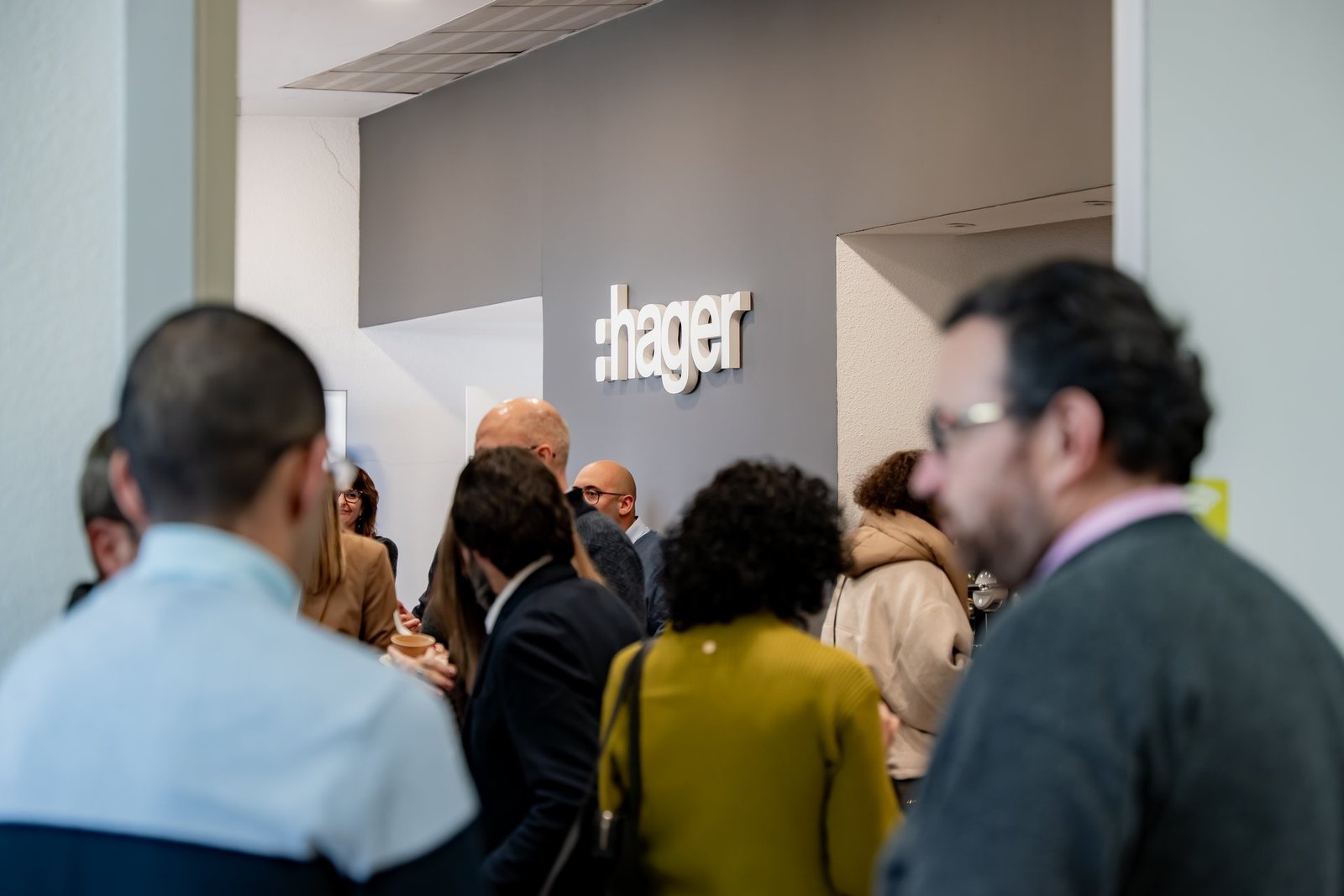 Asistentes al evento Kickoff de Hager. El logo de la empresa se ve en la pared gris de fondo, con personas interactuando en primer plano.